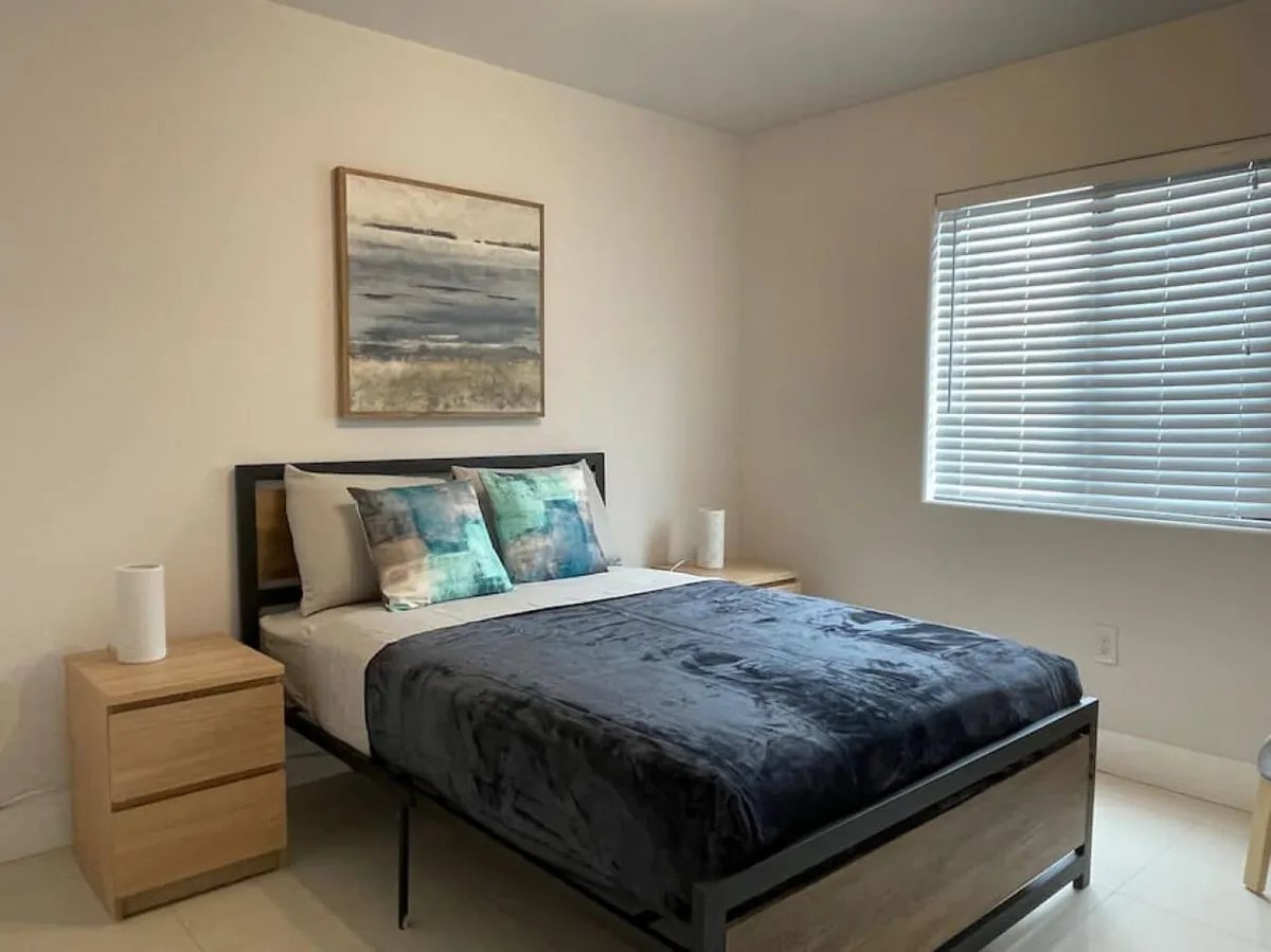 A tranquil bedroom scene featuring a well-made queen bed with plush pillows and stylish artwork above the headboard. Nightstands with soft lighting flank the bed, creating a cozy and peaceful atmosphere. The overall feel is calming and welcoming, ideal for restful sleep.