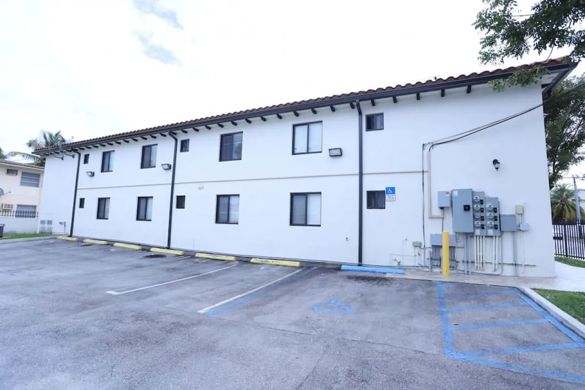 This image shows the exterior of the building with a clear view of the parking area situated directly in front. The building facade and several windows are visible, along with cars parked conveniently close to the entry, emphasizing easy access.